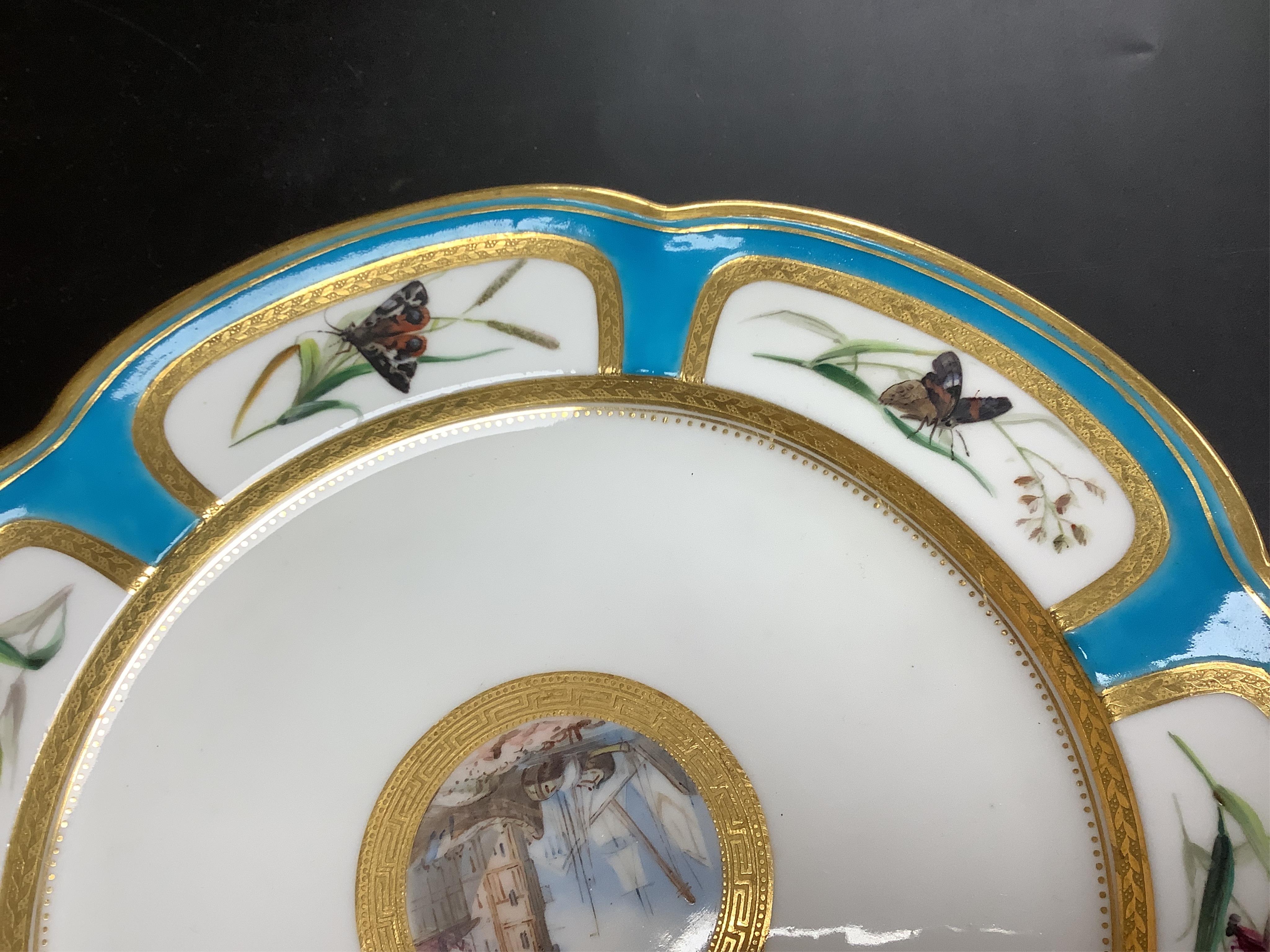 A Minton turquoise and gilt cabinet plate, decorated with butterflies and central continental harbour scene, 24cm diameter.